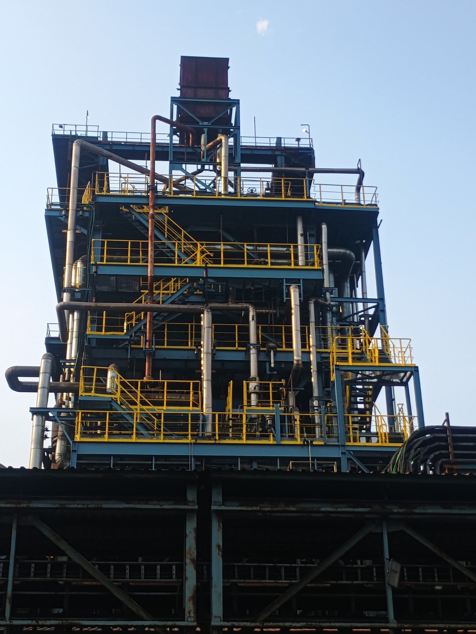 Multi-level industrial process tower with blue and yellow painted platforms, stairways and piping
